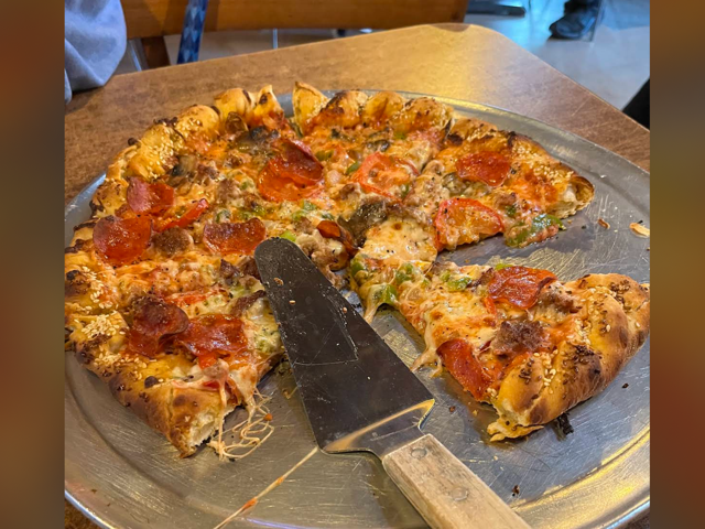Loaded supreme pizza with pepperoni, sausage and green chile on a metal pan with a server