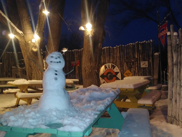 Snowman built on a turquoise picnic table on the snowy patio at dusk