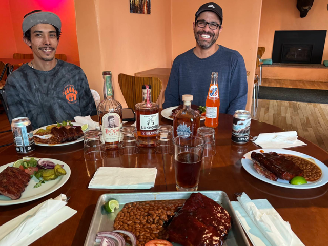 Friends around a table full of ribs, beans and drinks in the dining room