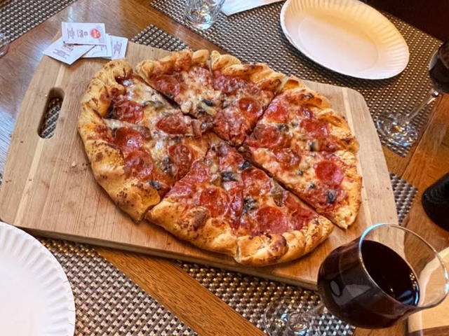 Pepperoni and mushroom pizza on a wooden board with a glass of red wine