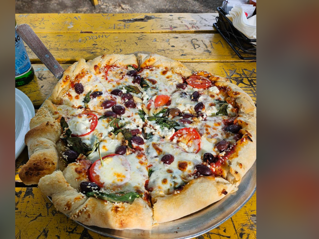 Greek pizza with kalamata olives, feta, tomato and spinach on a carved yellow table