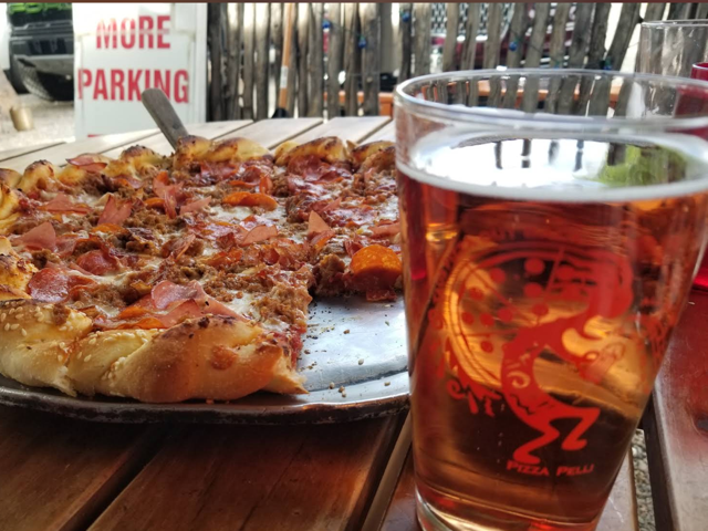 Meat pizza on the patio next to a Kokopelli-etched pint of beer
