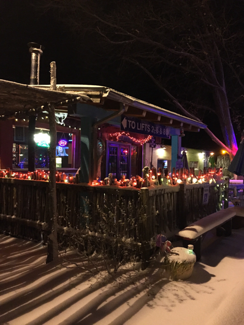 Snowy winter night on the patio with holiday lights, luminarias along the fence and a To Lifts sign
