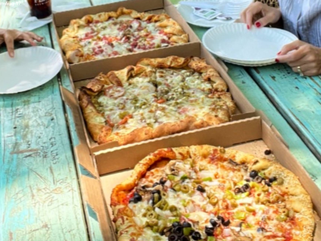Three open pizza boxes on a turquoise picnic table ready to share