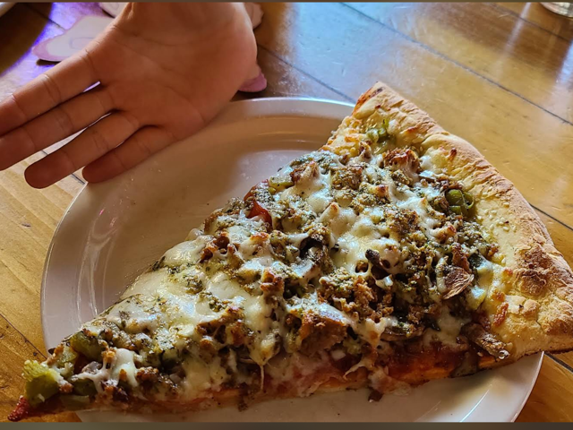 Big slice of pesto, sausage and green chile pizza on a white plate