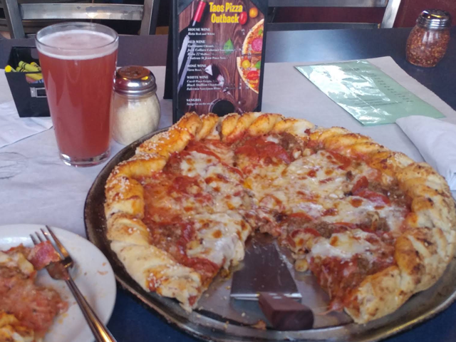 Sausage pizza on a pan beside a pint of beer and the Taos Pizza Out Back wine menu
