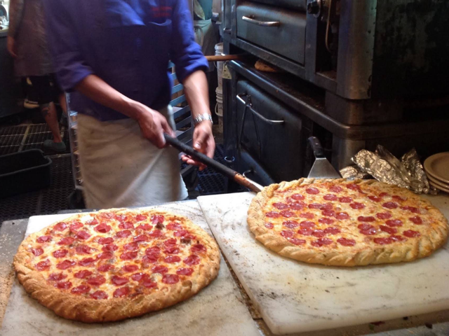 Two fresh pepperoni pizzas coming off the peel in the kitchen