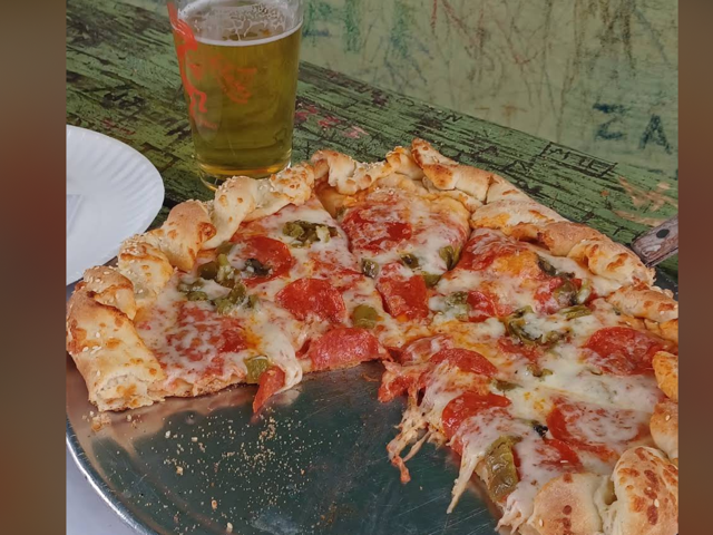 Pepperoni and green chile pizza with a pint of beer on a carved green table