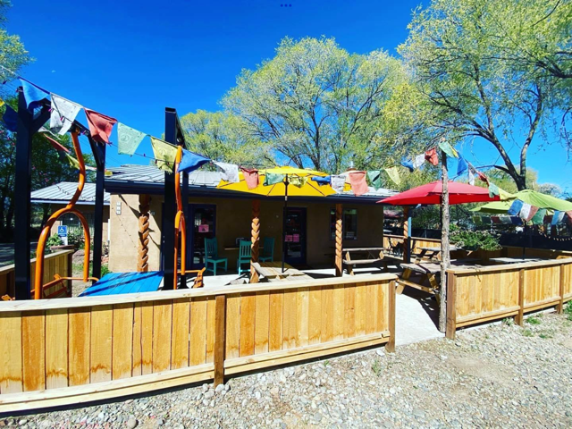 Sunny patio strung with Tibetan prayer flags and colorful umbrellas behind a wood fence