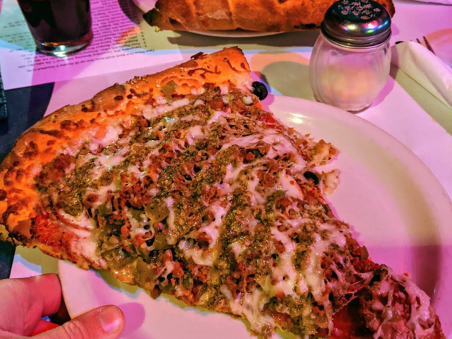 Huge slice of pesto and green chile pizza held over a plate