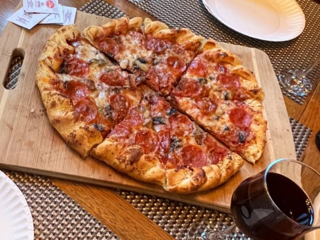 Pepperoni and mushroom pizza sliced on a wooden board with a glass of red wine