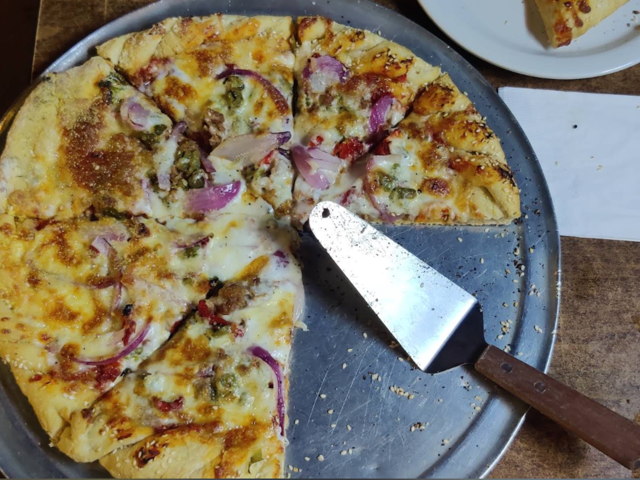Veggie pizza with red onion and green chile, one slice lifted off the pan