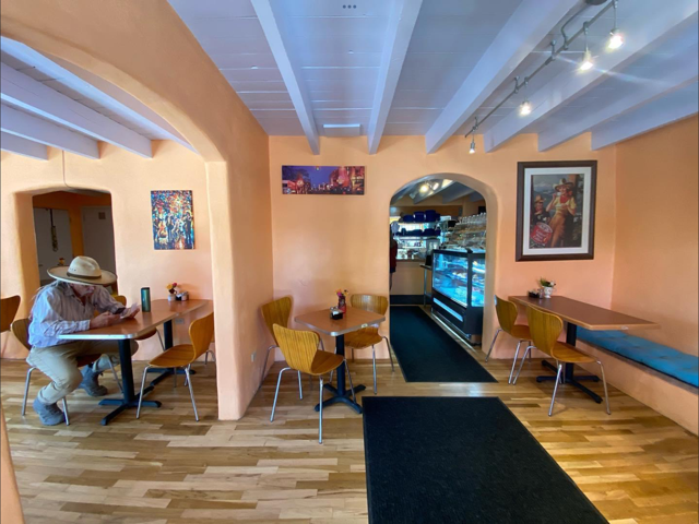 Bright dining room with peach adobe walls, white viga ceiling and local artwork