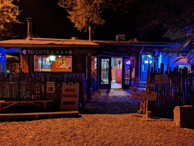 Taos Pizza Out Back storefront glowing blue at night beside the To Lifts sign