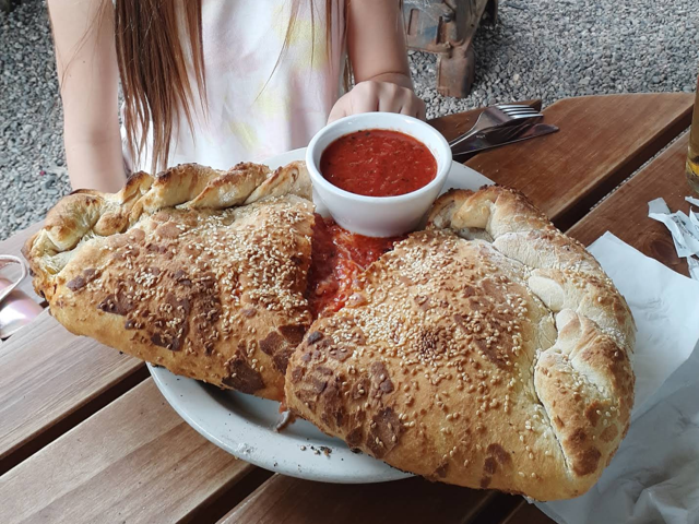 Golden sesame-crust calzone split open with a cup of marinara on the patio