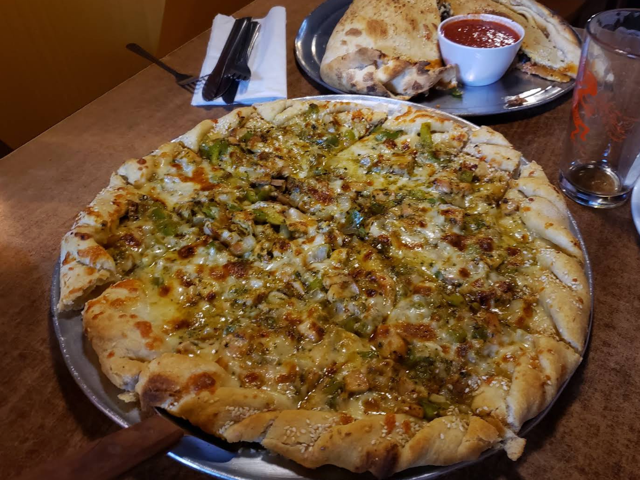 Green chile chicken pizza on a metal pan beside a calzone with marinara