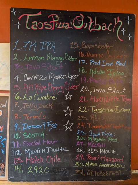 Colorful chalkboard listing 31 draft and bottled beers at Taos Pizza Out Back