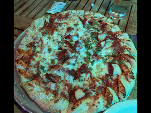 Bacon, chicken and green chile pizza on the patio table under evening light
