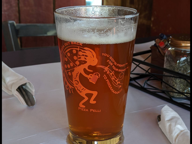 Pizza Pelli pint glass full of amber beer on a white tablecloth