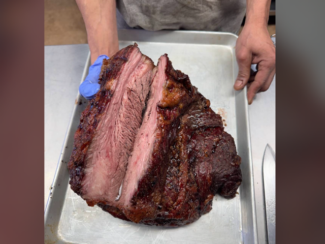 Whole smoked brisket being sliced on a sheet pan in the kitchen
