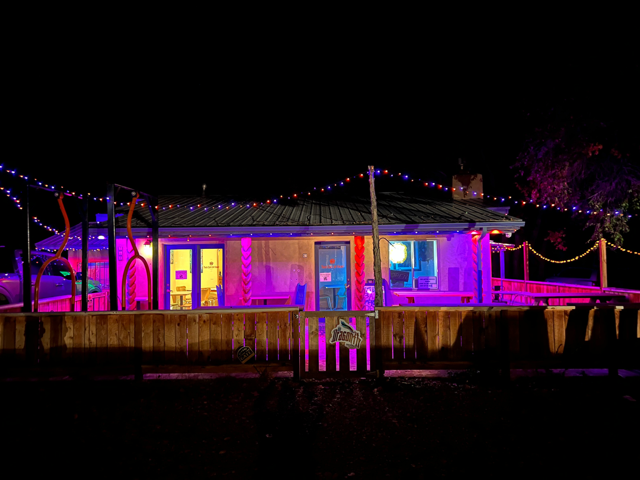 Adobe building glowing pink and purple at night with holiday lights along the roofline